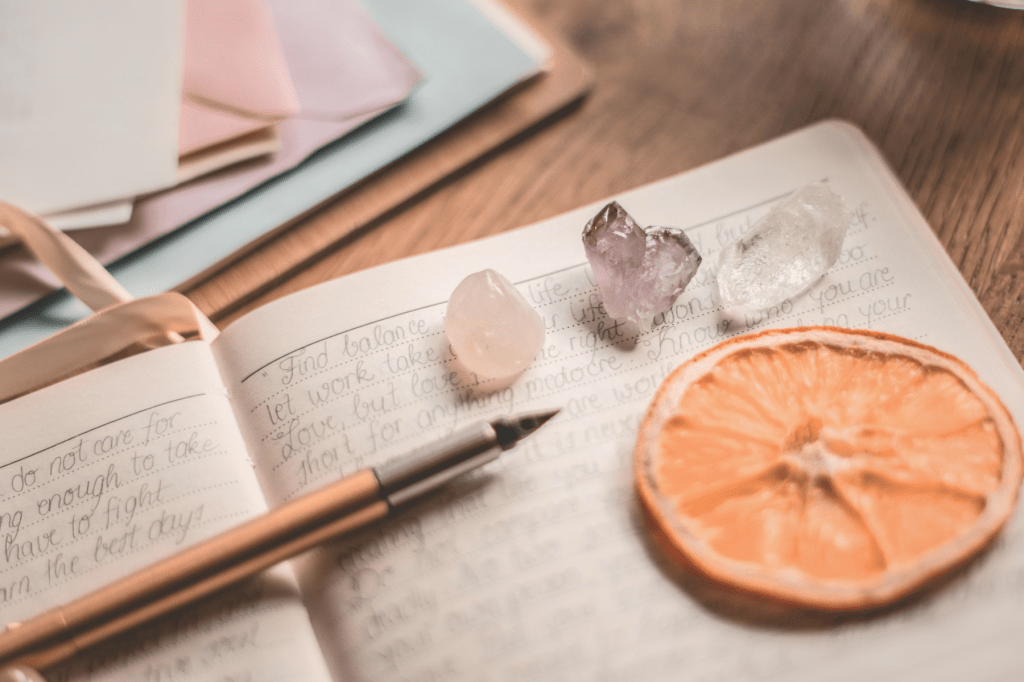 A mindful journaling scene with a fountain pen, healing crystals, and a dried orange slice, symbolising reflection, gratitude, and balance in holistic stress management.