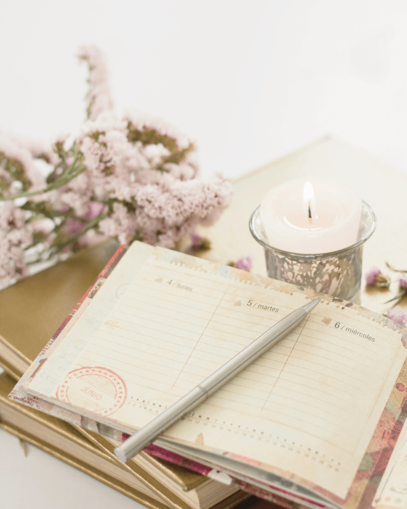 An open journal beside a lit candle and delicate flowers, symbolising reflection, mindfulness, and the practice of self-awareness.