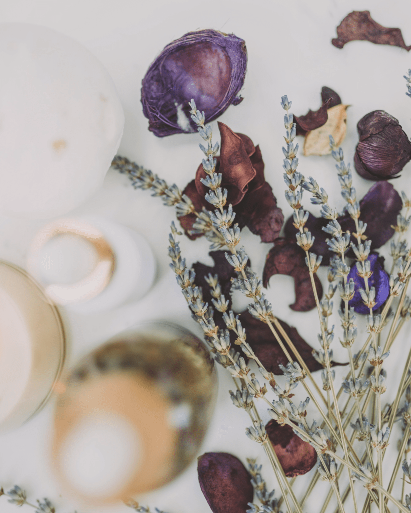 A serene flat lay featuring lavender stems, rose petals, and candlelight on a neutral surface. The composition conveys calm, mindfulness, and healing, representing the quiet balance of nervous system regulation and embodied presence within trauma recovery.
