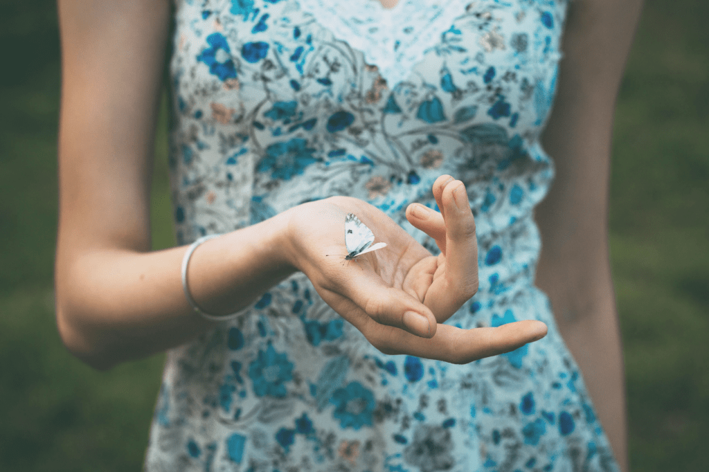 A person gently holding a butterfly in their open hand, symbolising tenderness, trust, and transformation born from safety.