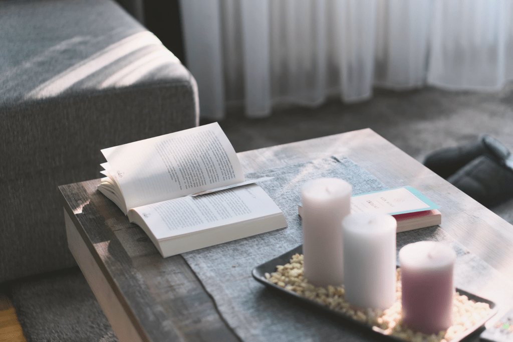 Open book and lit candles on a wooden table in soft natural light, symbolising calm, reflection, and nervous system regulation rituals.