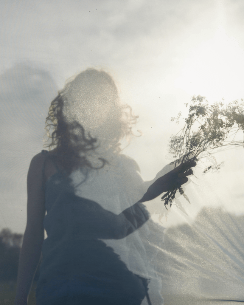 Soft, dreamlike image of a woman holding wildflowers in gentle light, symbolising emergence from survival, healing, and the awakening of self-trust.