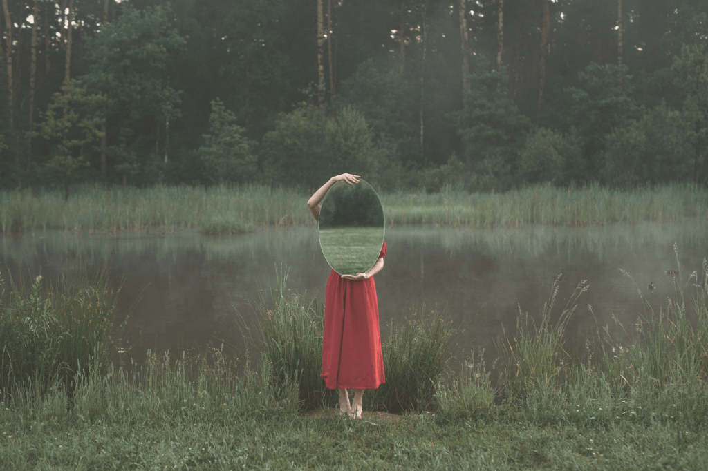 Person holding a mirror in nature, symbolising self-reflection, identity healing, and reclaiming wholeness after trauma.