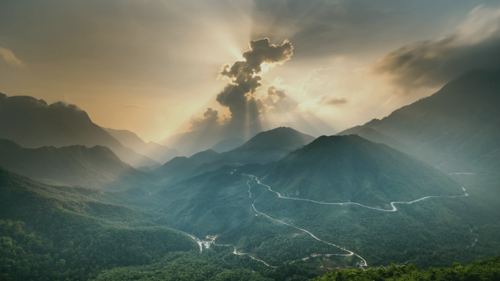 Sunlight breaking through clouds over winding mountain paths, symbolising personal growth, self-mastery, and the journey towards living wisdom; reflecting the transformative online sessions and holistic programmes offered by Metamorphosis Wellness.