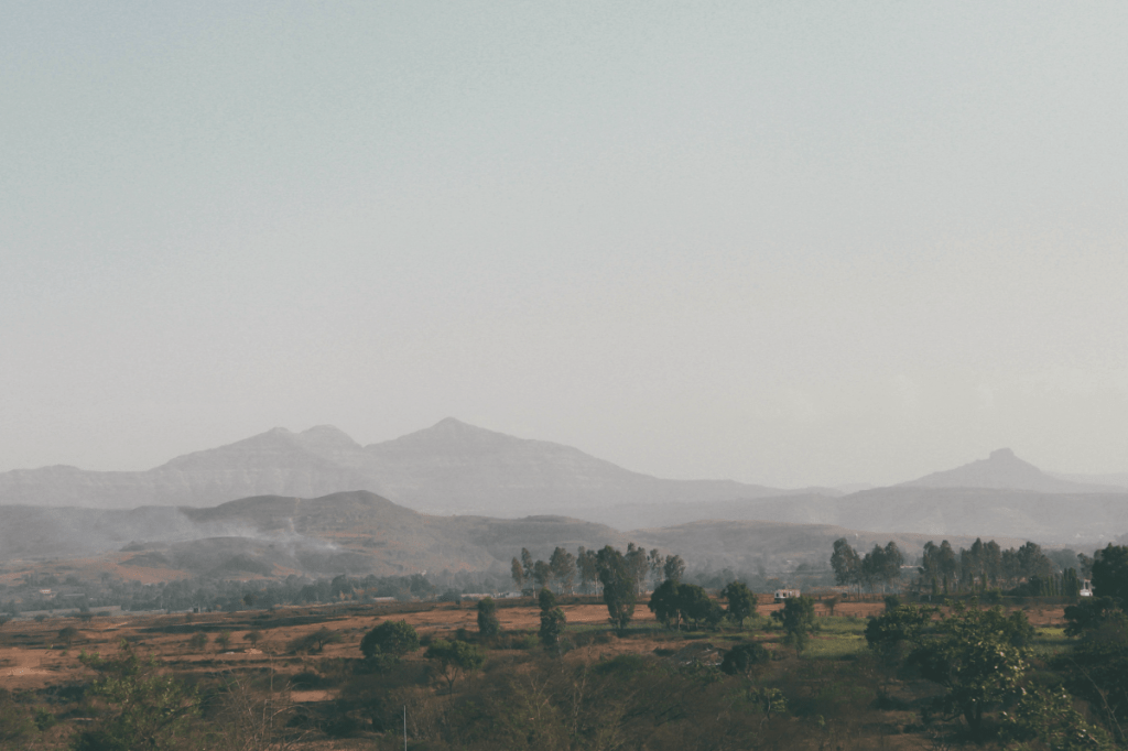 Distant landscape with fields and fog-covered mountains symbolising nervous system regulation as the capacity to return after activation, not a permanent state of calm.