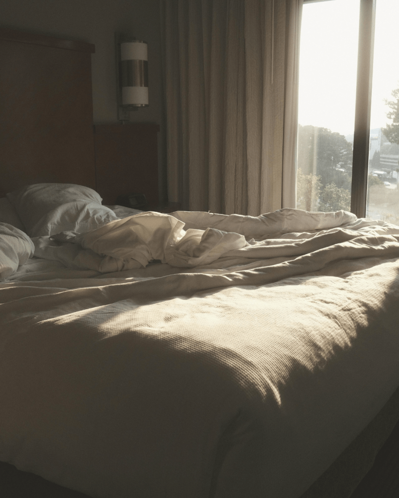 Unmade bed in a quiet bedroom with soft morning light through a window