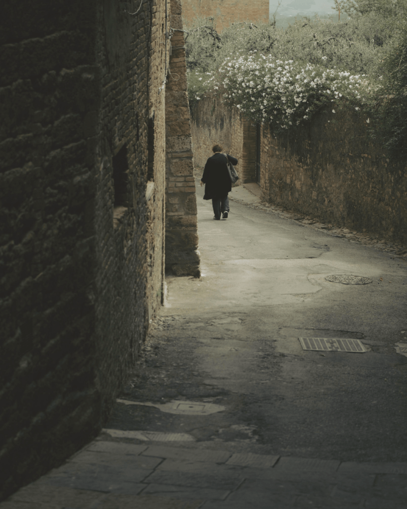 Person walking alone down a narrow street in an old town setting.