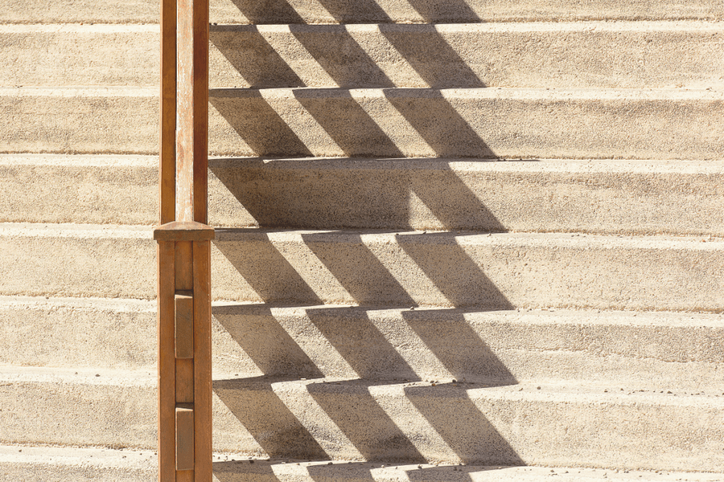 Concrete steps with a wooden railing, sunlight casting shadows across the stairs.