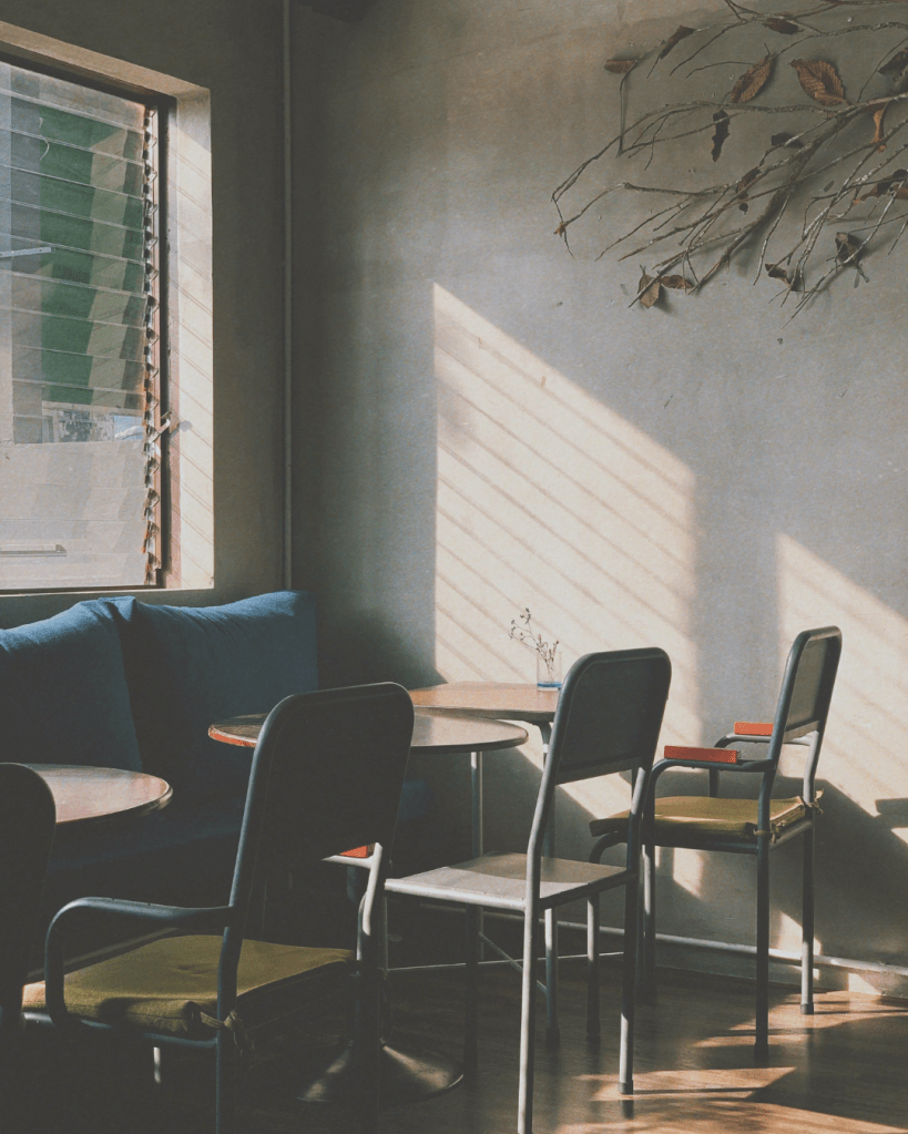 Quiet café interior with empty chairs and soft daylight entering through a window, showing stillness and reduced activity
