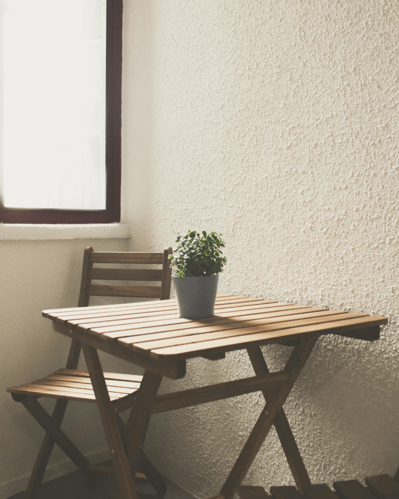 Small wooden table and chair by a window, symbolising containment, neutrality, and the everyday environments where survival responses quietly develop.