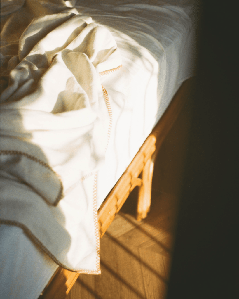 Sunlit bed with rumpled sheets in a quiet room, illustrating difficulty resting due to nervous system dysregulation after trauma