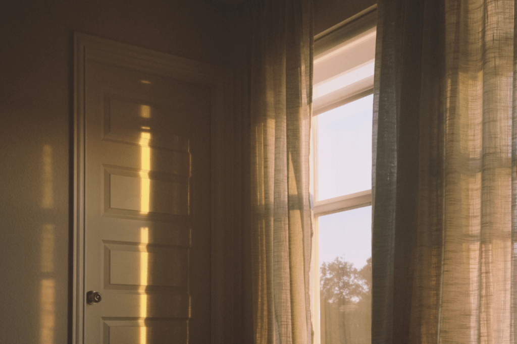 Sunlight entering through curtains in a quiet room symbolising emotional recovery, reclaiming identity and rebuilding safety after coercive control.