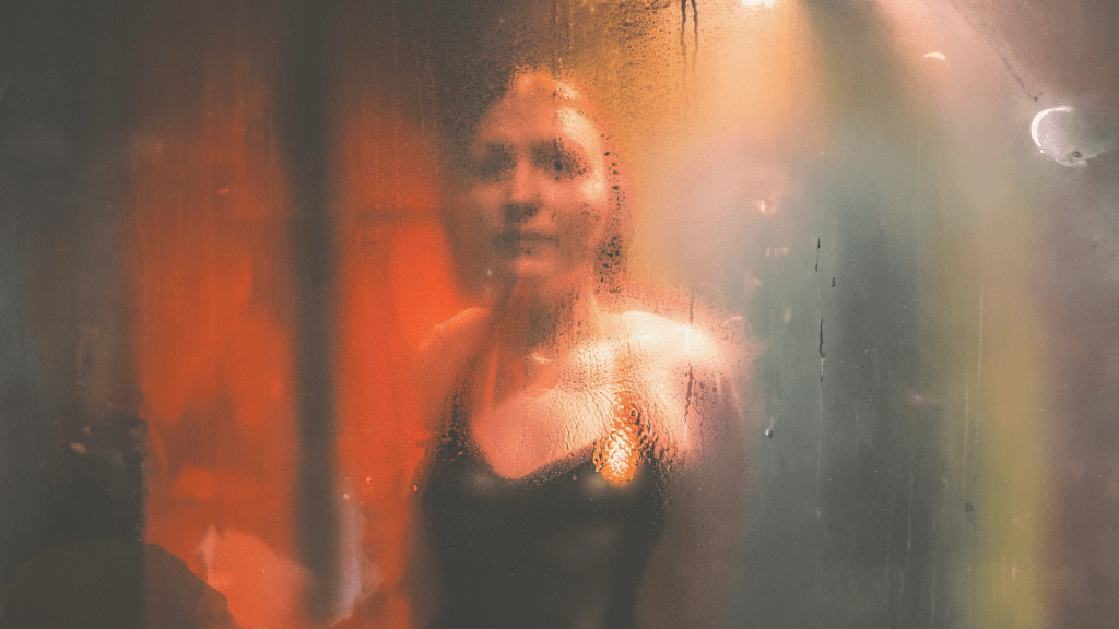 Blurred female figure behind fogged glass symbolising identity confusion, emotional dissociation and loss of self after coercive control and psychological abuse.