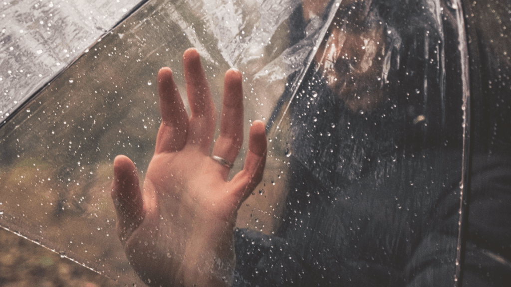 Hand pressed against a rain-speckled transparent barrier, representing why insight alone does not heal trauma and the process of nervous system integration after emotional abuse.